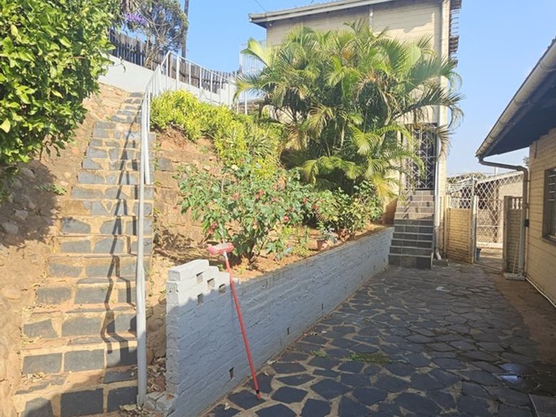 Rear exterior view featuring a stone-paved pathway, stone stairs with metal handrails, and a tiered garden area with a retaining wall.