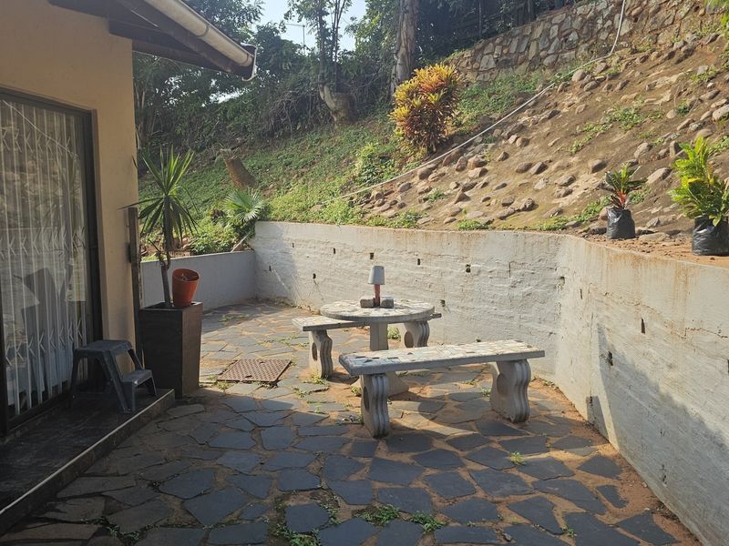 Outdoor patio area featuring stone paving and a concrete retaining wall, providing access to the home via a sliding glass door.