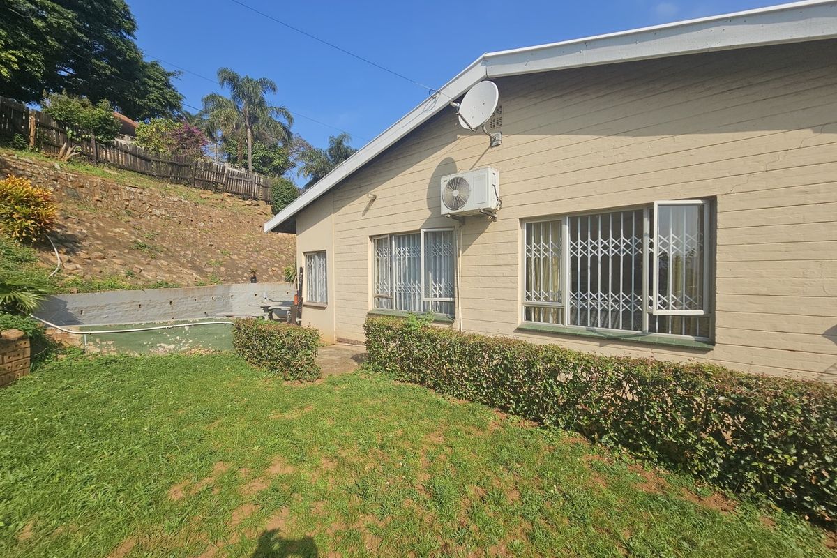 Rear exterior view of the house featuring a lawn, retaining wall, and security bars on the windows.