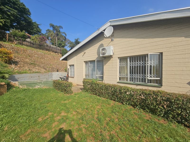 Rear exterior view of the house featuring a lawn, retaining wall, and security bars on the windows.