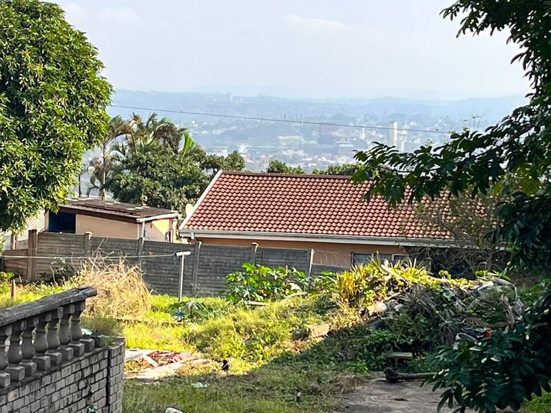 An elevated view overlooking a residential area, featuring a tiled roof property, precast boundary wall, and surrounding garden space.