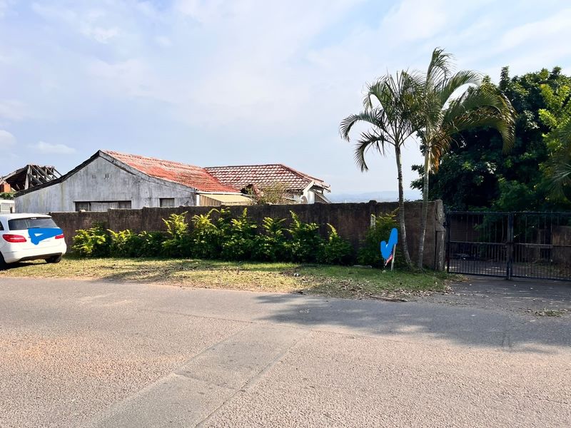 Street view of the property showing the front boundary wall, metal gate, and the main house structure with a weathered tiled roof.
