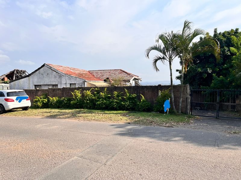 Street view of the property showing the boundary wall, metal gate, and the main dwelling with visible roof deterioration.