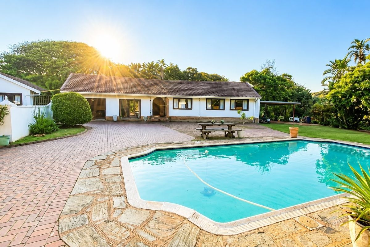 Rear exterior view of the house featuring a swimming pool, paved patio area, and well-maintained garden surroundings.