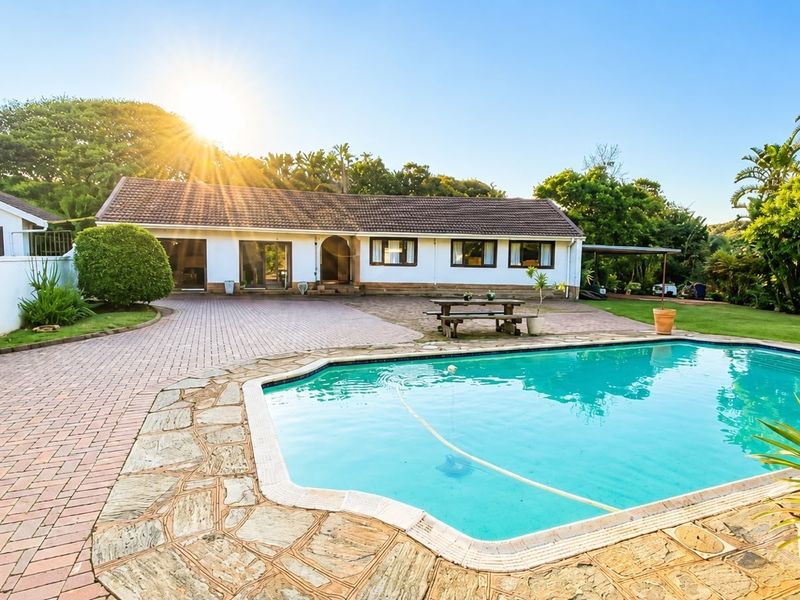 Rear exterior view of the house featuring a swimming pool, paved patio area, and well-maintained garden surroundings.