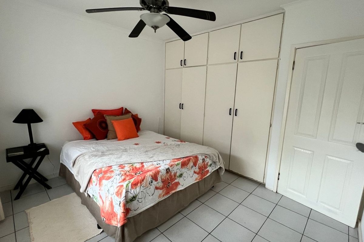 A functional bedroom featuring tiled flooring, a ceiling fan, and ample built-in cupboard storage space.