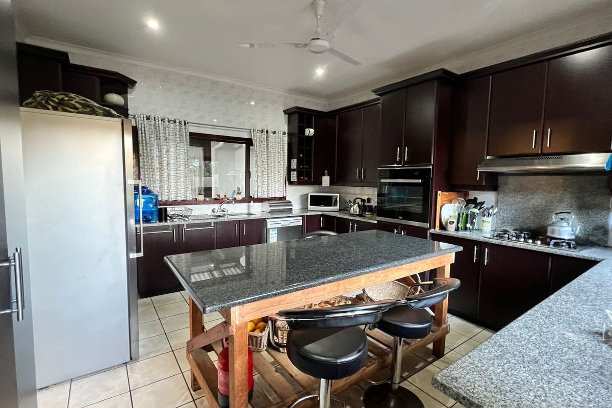 A functional kitchen featuring dark wood cabinetry, granite countertops, a built-in oven, and a central island with seating.