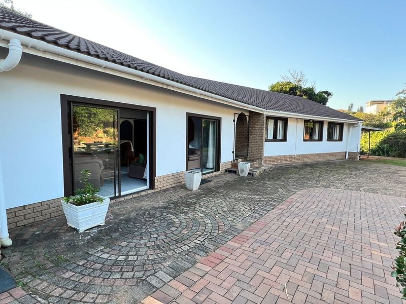 Rear exterior view of the house featuring a paved patio area, sliding glass doors, and a tiled roof.