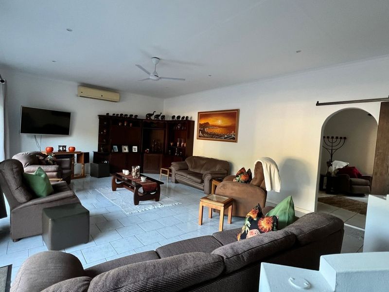 Spacious living room featuring tiled flooring, a ceiling fan, wall-mounted air conditioning, and an arched doorway leading to adjacent areas.