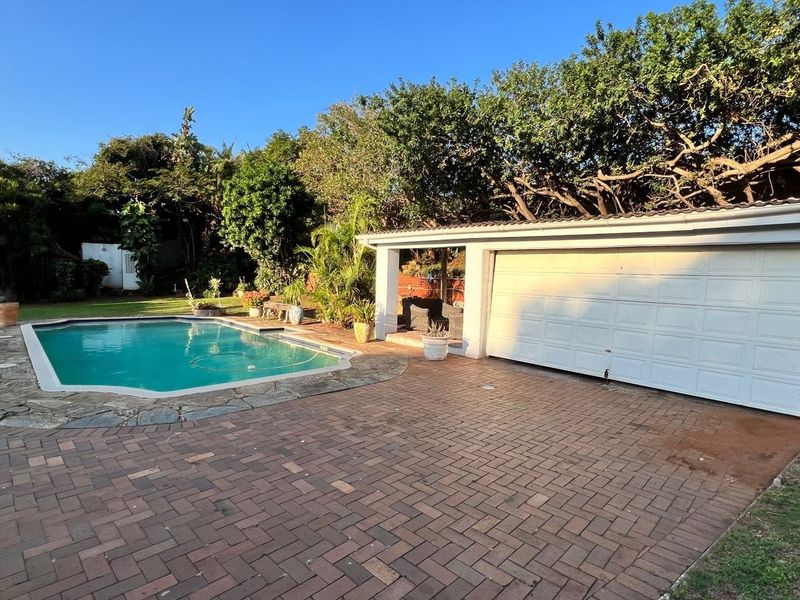 Outdoor entertainment area featuring a swimming pool with stone coping, paved patio space, and an attached garage with a white sectional door.