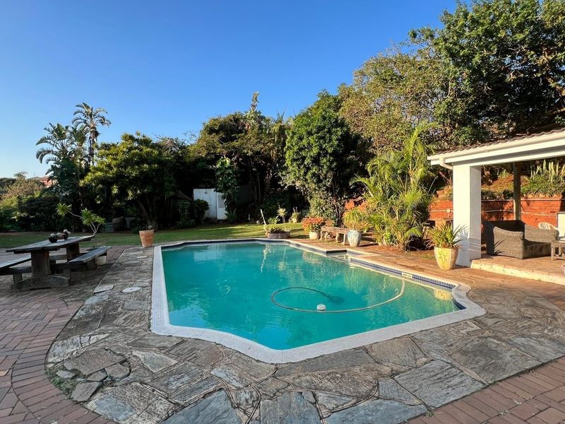Outdoor pool area featuring a swimming pool, paved surround, and a covered patio space set within a landscaped garden.