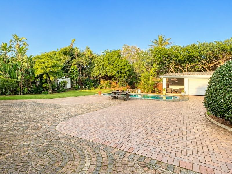 Spacious rear exterior featuring a large paved driveway, a swimming pool, and a well-maintained garden area with a detached garage.