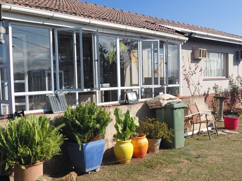 Rear view of the house featuring an enclosed sunroom, tiled roof, and a concrete retaining wall set against a garden area.