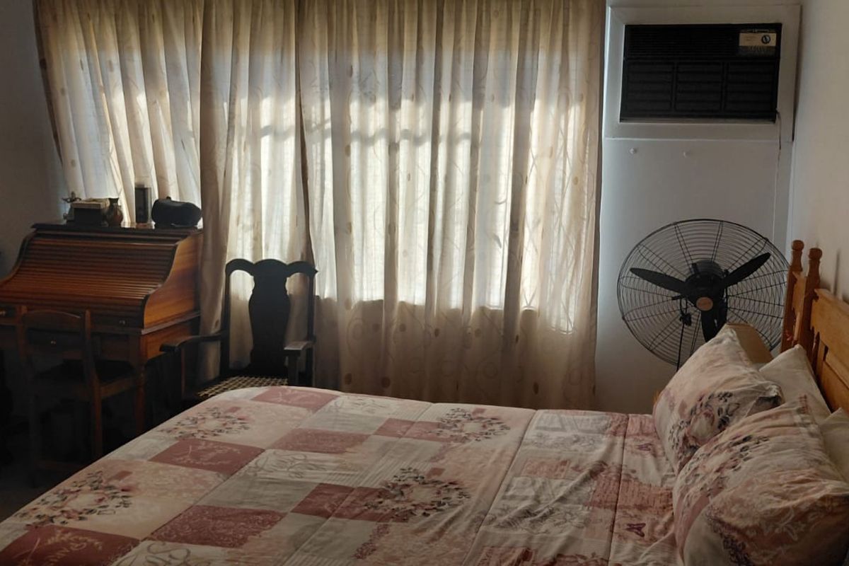 A bedroom featuring a window-mounted air conditioning unit and large windows covered by curtains.