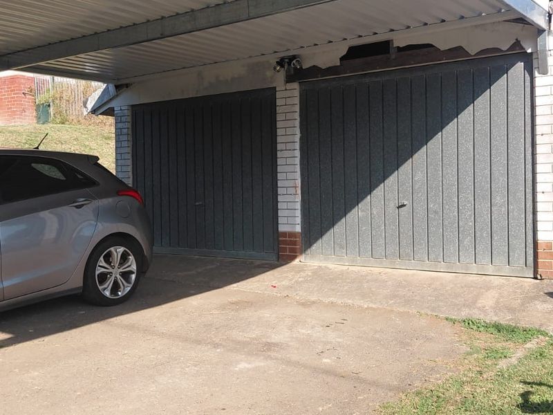 A double garage with an attached carport, featuring brick construction and metal garage doors, showing signs of exterior wear and maintenance requirements.