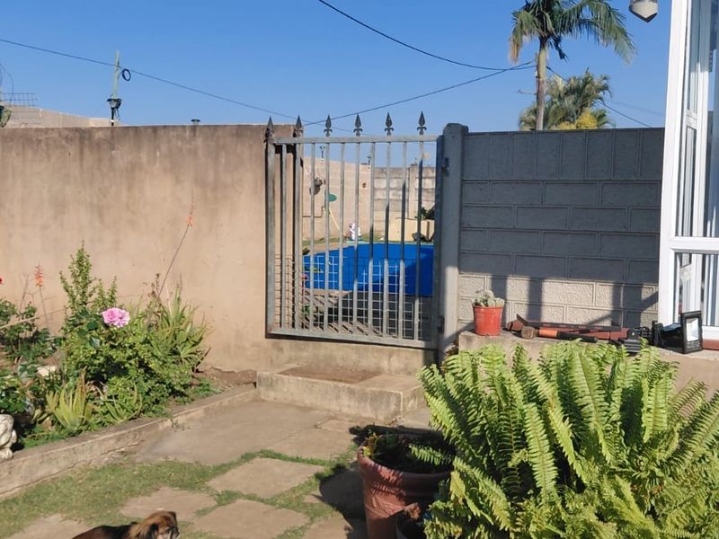 Rear garden area featuring a precast concrete boundary wall, metal security gate, and paved patio access to the main dwelling.