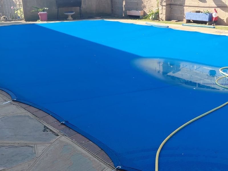 Outdoor swimming pool area featuring a blue safety cover and stone paved surround.