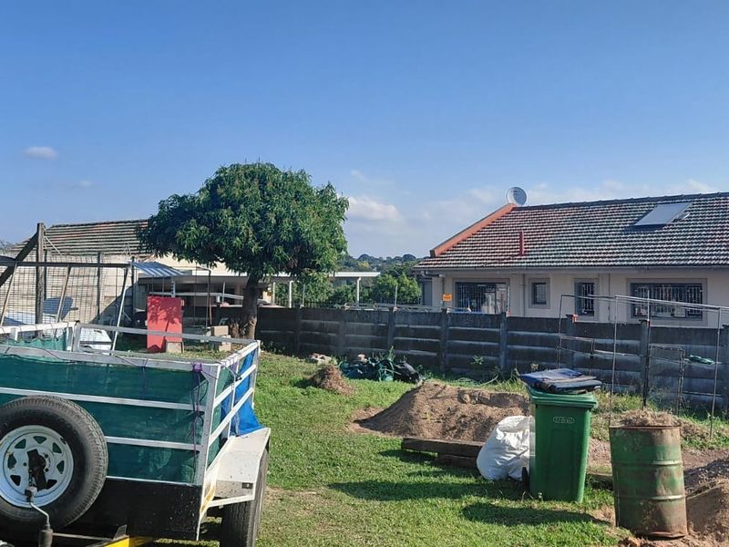 A view of the rear yard featuring a precast concrete boundary wall and a residential building with a tiled roof and solar water heater.