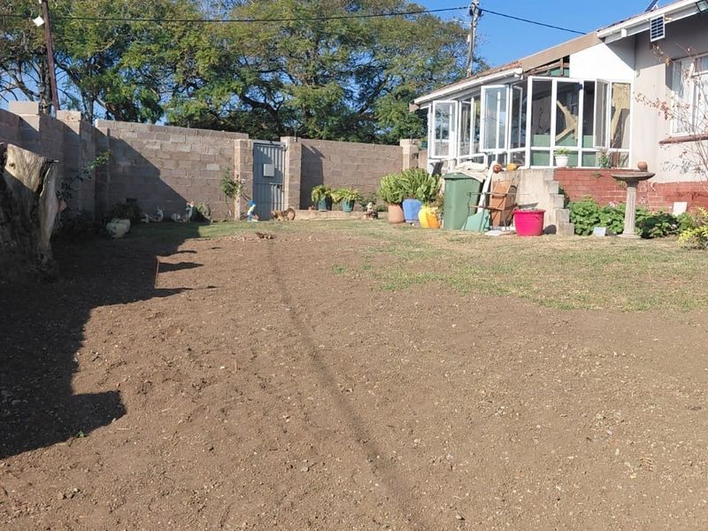 Rear garden area featuring a concrete block boundary wall, an enclosed patio structure, and an open yard space requiring landscaping.