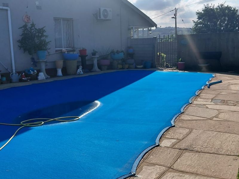 Outdoor pool area featuring a blue pool cover, paved surround, and boundary wall, adjacent to the rear elevation of the house.
