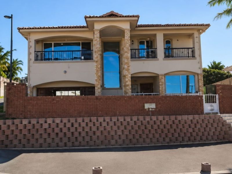 A two-story residential property featuring a brick retaining wall, stone facade accents, tiled roof, and upper-level balconies with metal railings.