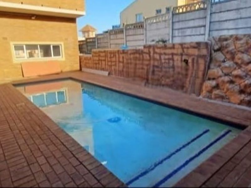 Outdoor pool area featuring brick paving, a decorative rock retaining wall, and a precast concrete boundary wall.