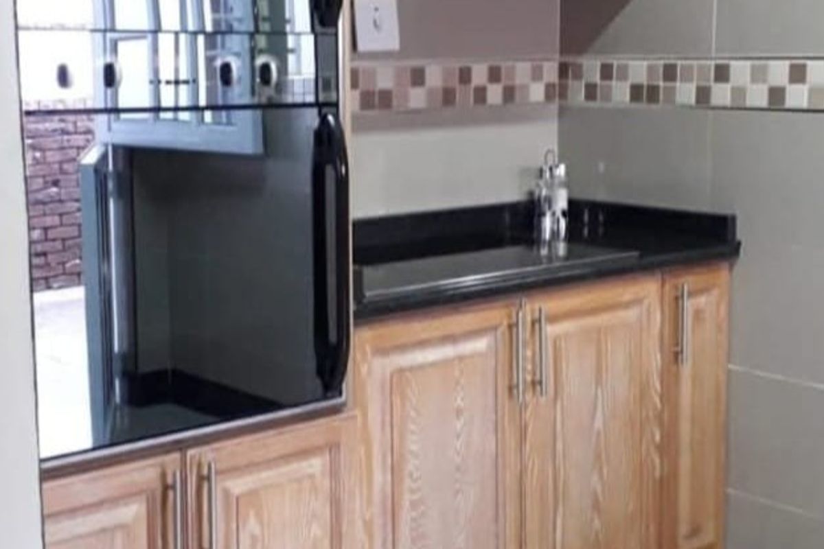 A functional kitchen area featuring wooden cabinetry, a black granite countertop, and a built-in oven with a decorative tiled backsplash.