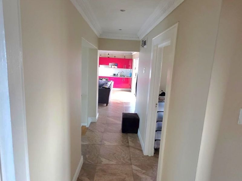 A neutral-toned hallway featuring tiled flooring and crown molding, providing a clear transition through the home toward the open-plan living and kitchen area.