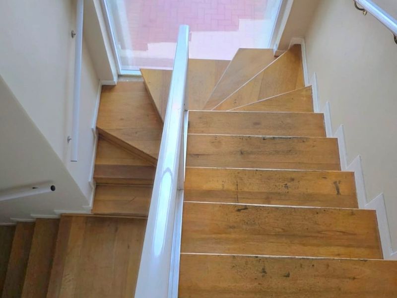 A wooden staircase with a handrail leading to a glass door, showing signs of wear on the treads.