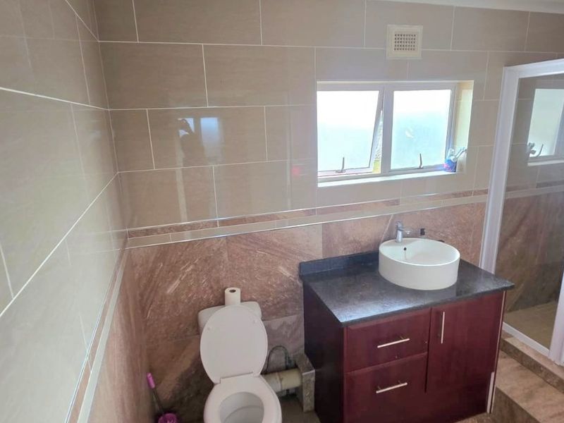 A functional bathroom featuring tiled walls, a vanity cabinet with a vessel sink, a toilet, and a separate shower enclosure.