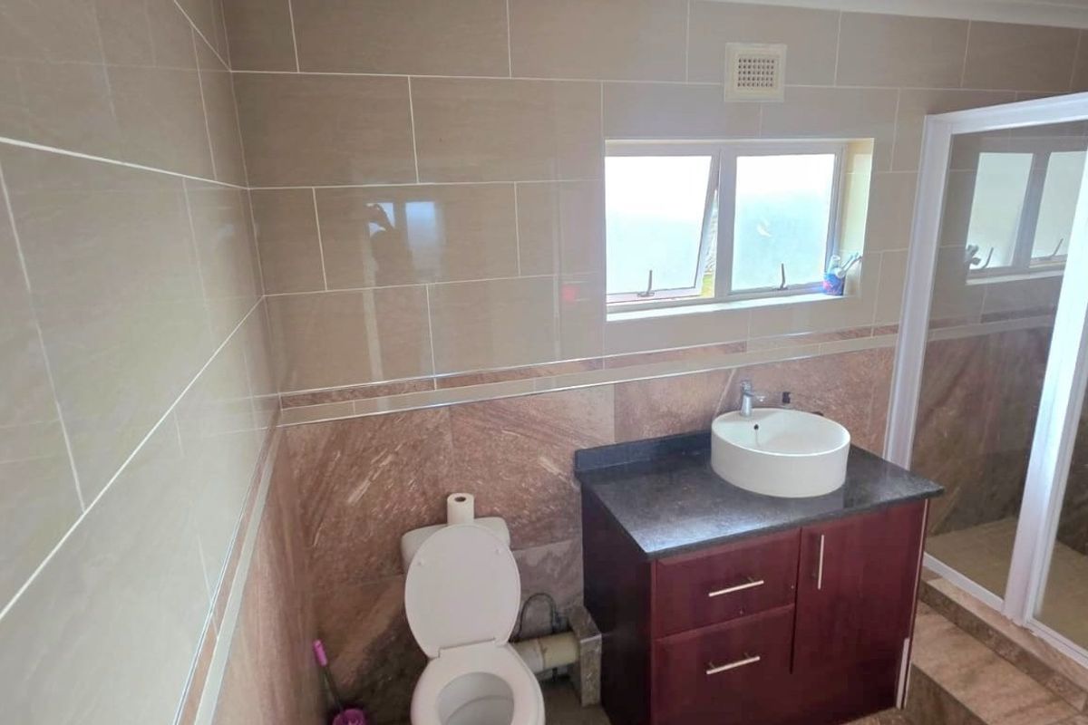 A functional bathroom featuring tiled walls, a vanity cabinet with a vessel sink, a toilet, and a separate shower enclosure.