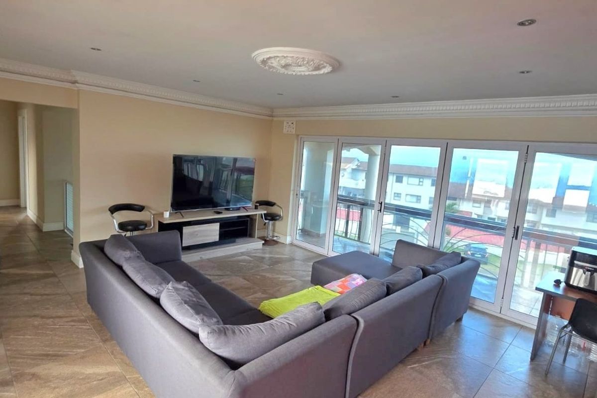 Spacious living room featuring large sliding glass doors, tiled flooring, recessed lighting, and decorative crown molding, offering access to an outdoor balcony area.