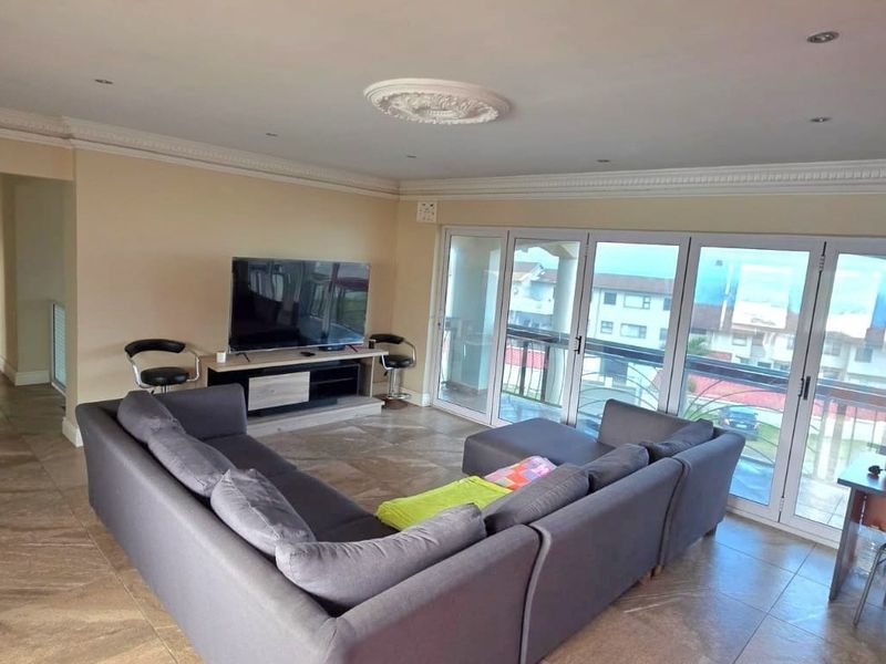Spacious living room featuring large sliding glass doors, tiled flooring, recessed lighting, and decorative crown molding, offering access to an outdoor balcony area.