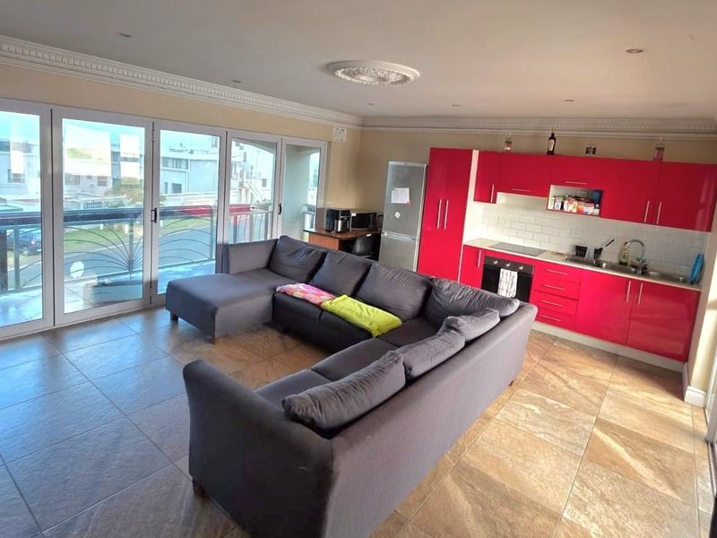 Open-plan living area featuring a modern kitchen with vibrant red cabinetry, tiled flooring, and large sliding doors leading to a balcony.