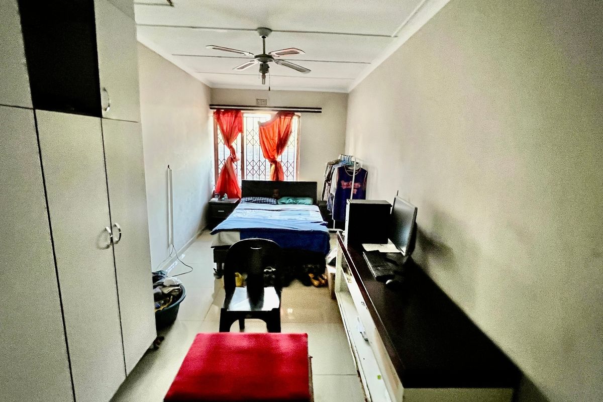 A functional bedroom featuring built-in cupboards, a ceiling fan, and security bars on the window.