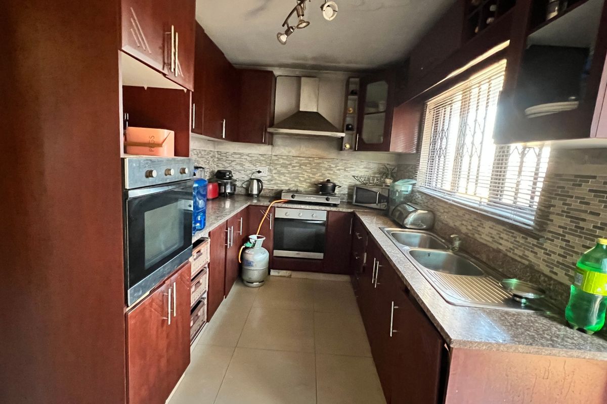 A functional kitchen featuring dark wood cabinetry, a built-in oven, gas hob, extractor fan, and a stainless steel sink with a tiled backsplash.