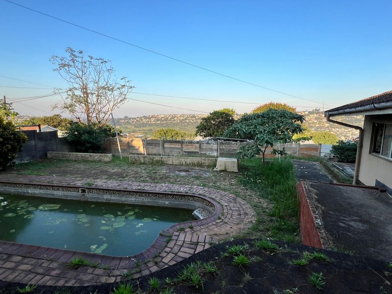 Outdoor pool area featuring a swimming pool with brick paving, retaining walls, and views of the surrounding neighborhood, requiring maintenance and landscaping.