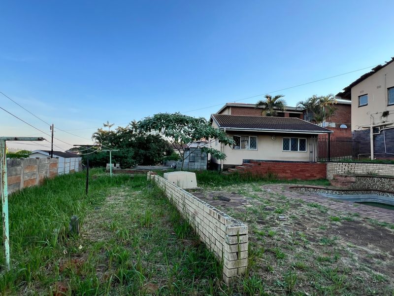 Rear exterior view of the property featuring a swimming pool, paved patio area, and a large garden space with boundary walling.