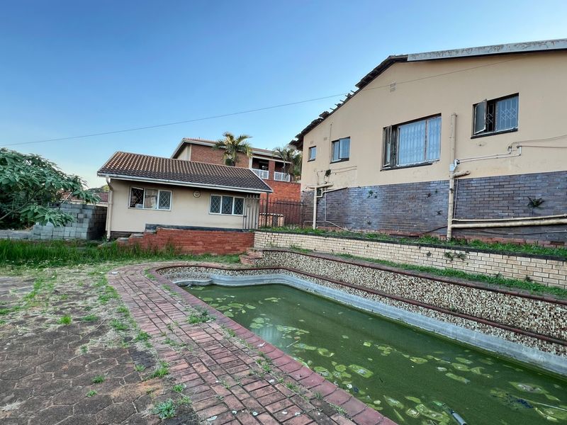 Rear exterior view featuring a neglected swimming pool, brick retaining walls, and paved surround, requiring significant maintenance and restoration.