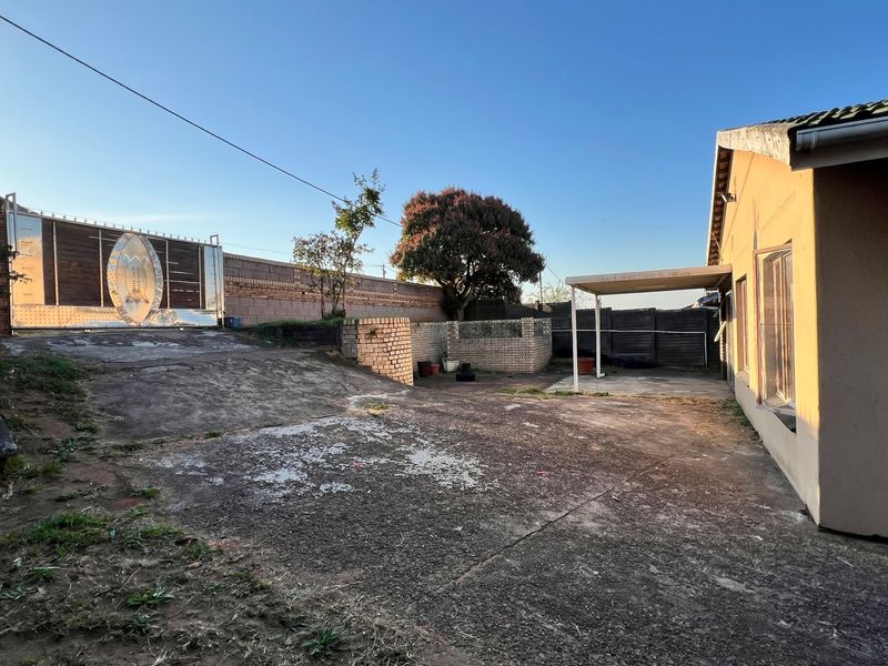 Rear exterior area featuring a concrete driveway, perimeter wall with sliding gate, and a covered patio structure.