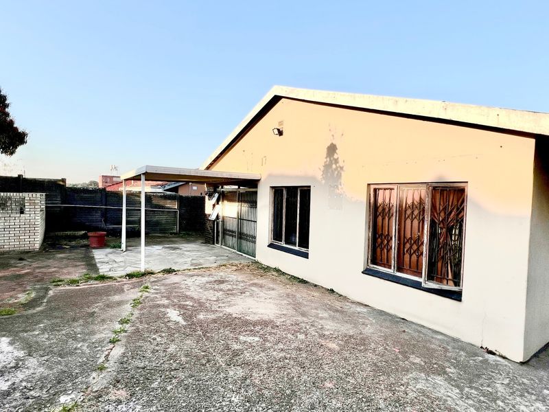 Rear exterior view of the house featuring a concrete patio area, security bars on windows, and a paved yard with boundary walling.