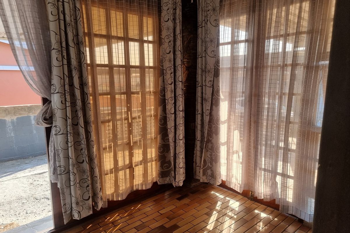 A bright, empty living area featuring warm wooden parquet flooring and large timber-framed french doors that allow for ample natural light.