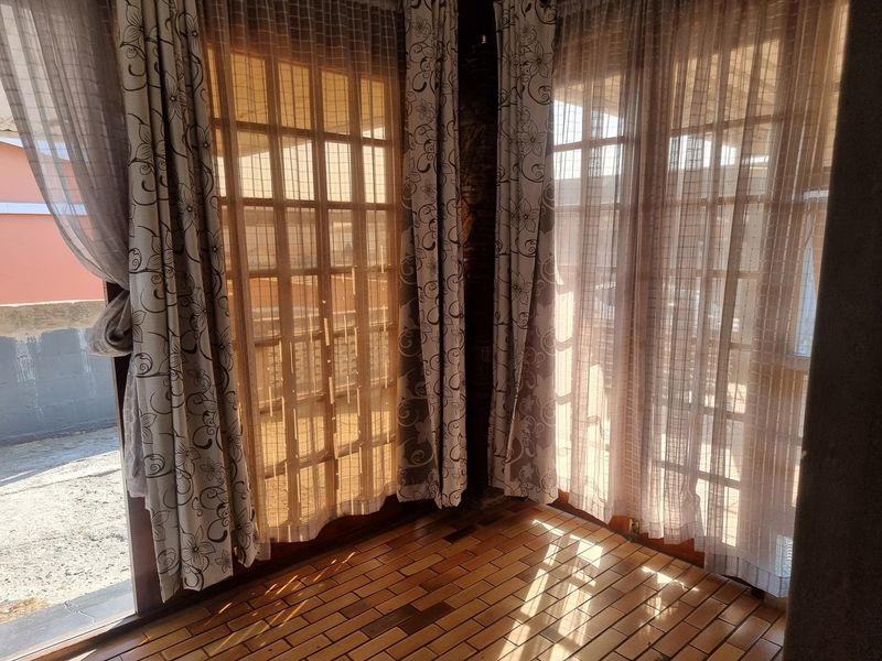 A bright, empty living area featuring warm wooden parquet flooring and large timber-framed french doors that allow for ample natural light.