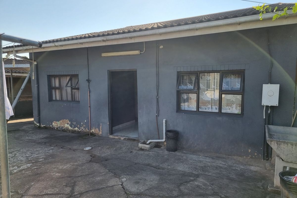 Rear exterior view of the house featuring a concrete apron, external utility sink, and dark painted walls showing signs of wear and peeling paint.