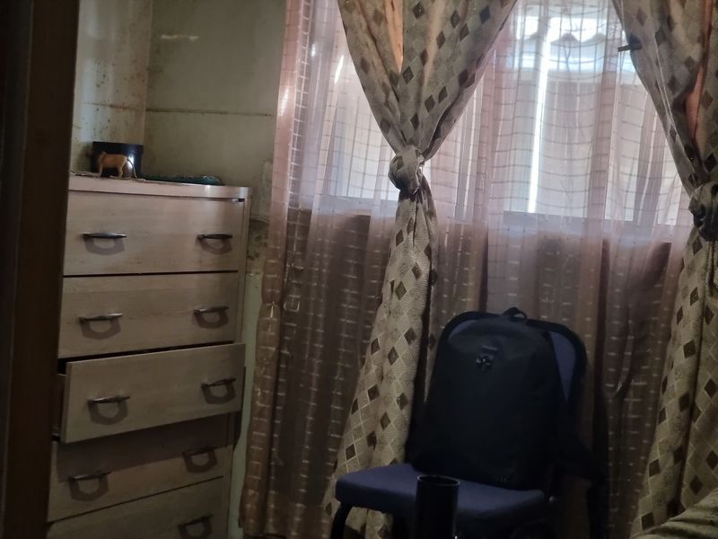 A bedroom interior featuring a window with curtains and visible wall surface deterioration requiring maintenance and repair.