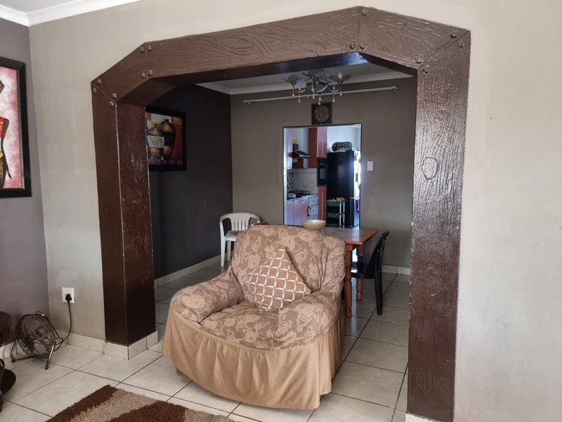 Open plan living and dining area featuring a prominent decorative archway and neutral ceramic floor tiles, connecting to the kitchen space.