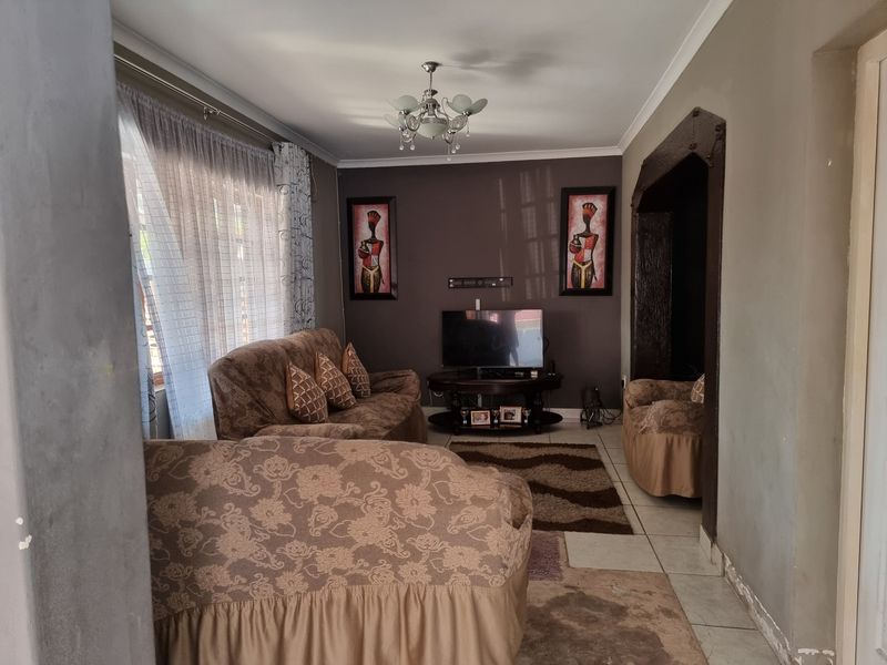 A living room featuring tiled flooring, a decorative archway, and a central chandelier, currently requiring cosmetic updates to the walls and flooring.