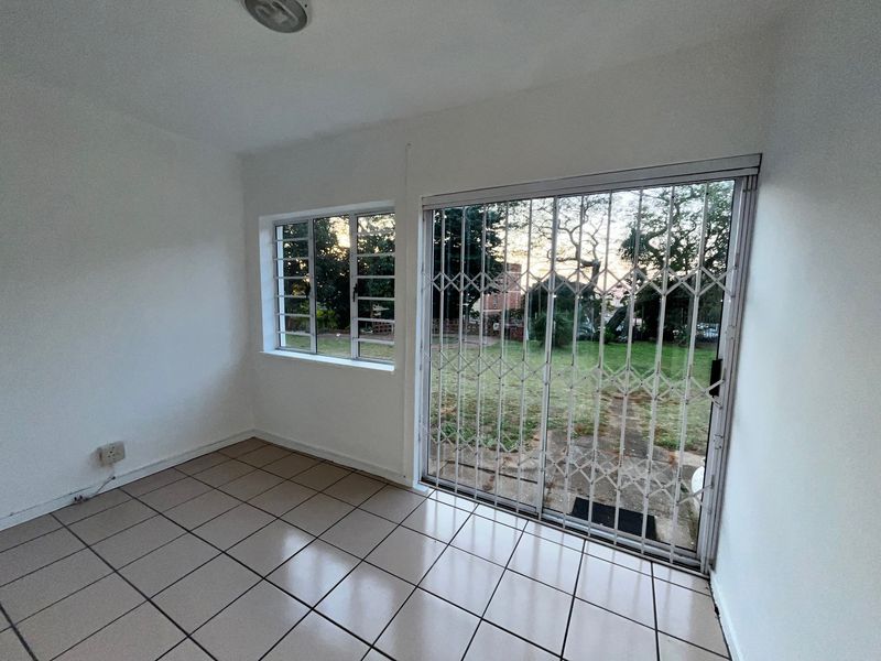 An empty living area featuring tiled flooring, a sliding glass door with a security gate, and a window overlooking the garden.