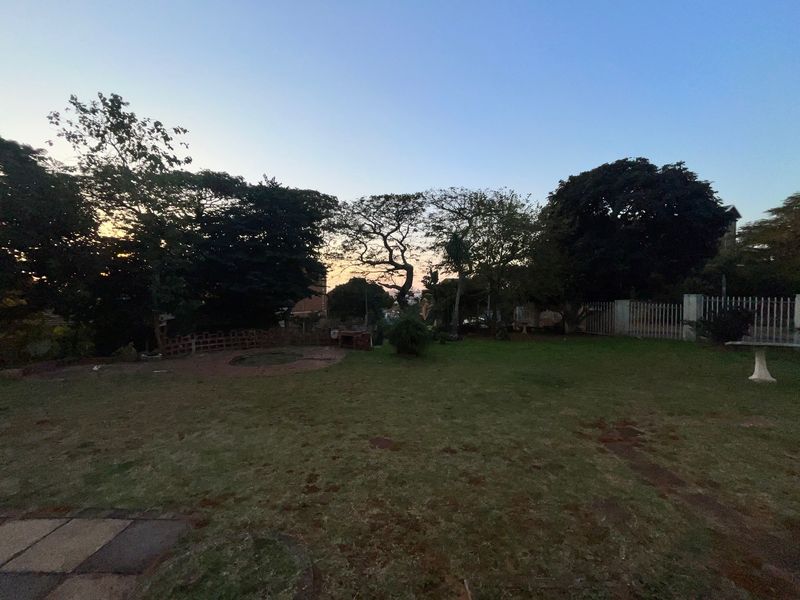 A spacious private garden area featuring mature trees, perimeter fencing, and a small paved section, offering potential for landscaping and outdoor development.