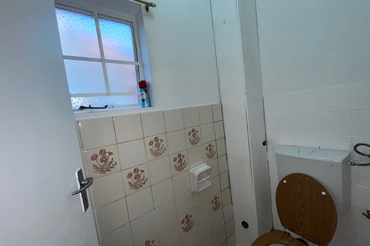 A compact bathroom featuring a toilet, tiled splashback, and an obscured glass window. The space requires cosmetic updates to modernize the finishes.